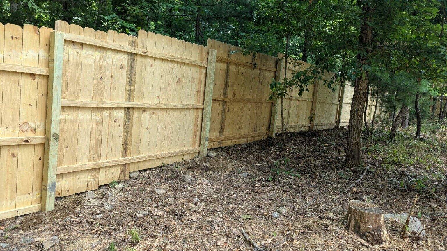 Wood privacy fence installed along wooded terrain